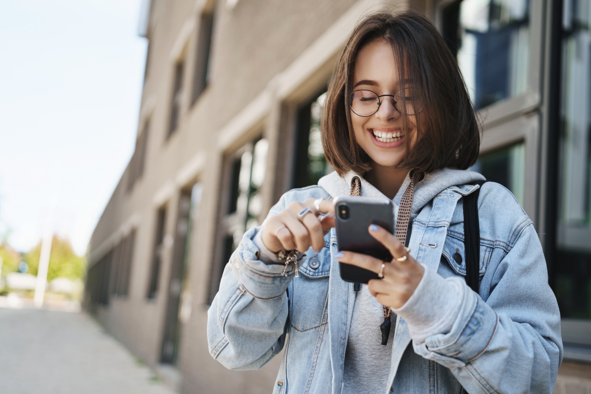 Colaboradora sorrindo enquanto usa o celular na rua